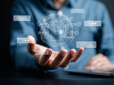 Symbolbild für künstliche Intelligenz: Digitale Darstellung eines Kopfes mit Zahnrädern über ausgestreckter Hand