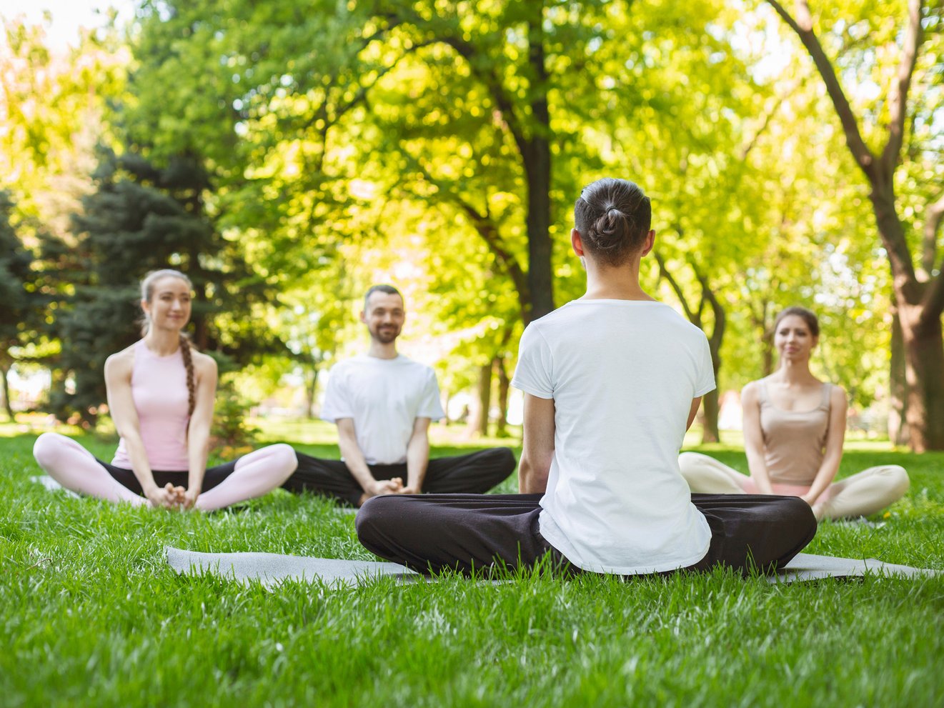 Yoga Dozentin und Teilnehmende sitzen auf den Rasen