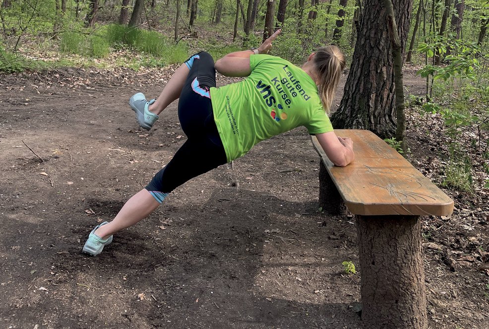 Liegendes X, Frau hat ein ausgestreckte Arm auf der Parkbank und ein angewinkeltes Bein zur Seite