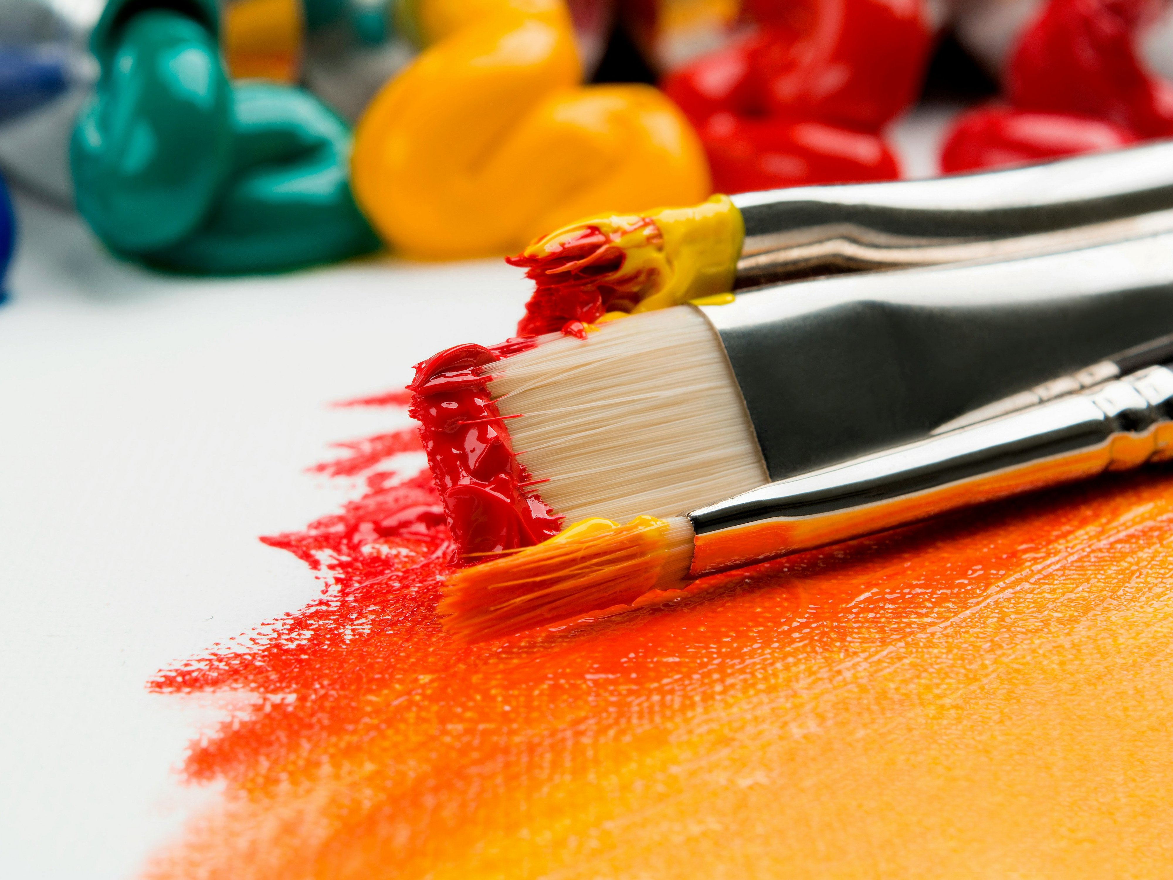 Zwei Pinsel tragen rote und orange Farbe auf ein weißes Blatt auf